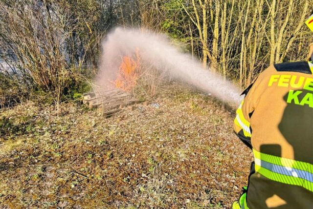 Ein Feuerwehrmann löscht mit Wasser aus einem Schlauch Flammen.