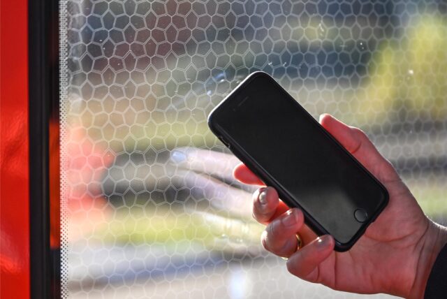 Eine Person hält ein Smartphone in der Hand und steht an einer Zugtür.