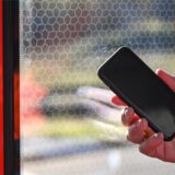 Eine Person hält ein Smartphone in der Hand und steht an einer Zugtür.
