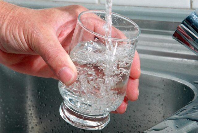 Eine Hand hält ein Glas unter einen Wasserhahn, während es mit Wasser gefüllt wird. Im Glas bilden sich zahlreiche Blasen.