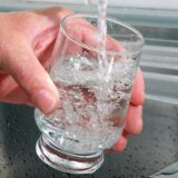 Eine Hand hält ein Glas unter einen Wasserhahn, während es mit Wasser gefüllt wird. Im Glas bilden sich zahlreiche Blasen.