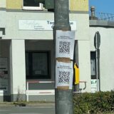 An einer Ampelkreuzung in Holzwickede hängen zwei selbstgemachte Schilder mit QR-Code – ohne erkennbare Herkunft oder Zweck.