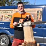 Andreas Stentrup mit einem Baumstamm, auf dem er seine Motorsäge ablegt.