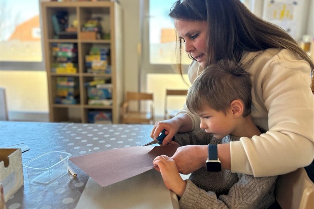 Erzieherin Iris Chatzopoulus bastelt in der Kita des Evangelischen Familienzentrums Aplerbecker Mark in Dortmund mit einem Kind an einem Tisch.