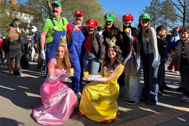 Die beiden Stufenleiter des Abi-Jahrgangs 2025 stehen als Mario und Luigi verkleidet mit Schülerinnen auf dem Schulhof des Heisenberg Gymnasiums. Sie sind auch als Mario und Luigi und als Daisy und Peach verkleidet.