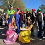Die beiden Stufenleiter des Abi-Jahrgangs 2025 stehen als Mario und Luigi verkleidet mit Schülerinnen auf dem Schulhof des Heisenberg Gymnasiums. Sie sind auch als Mario und Luigi und als Daisy und Peach verkleidet.