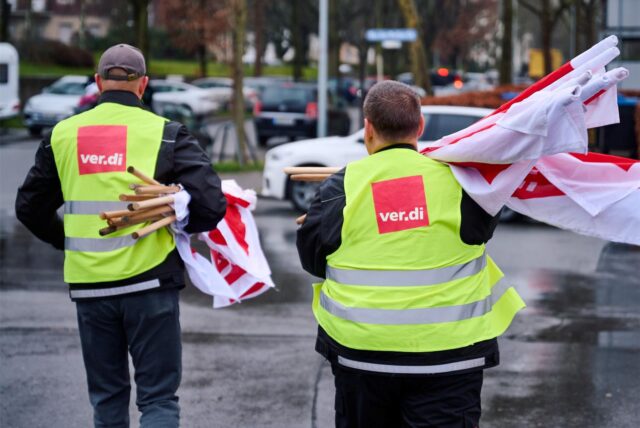 Zwei Männer mit Verdi-Westen und eingerollten Gewerkschaftsfahnen.