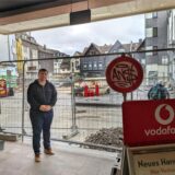 Ein Einzelhändler steht vor einem Bauzaun, der den Zugang zu seinem Geschäft verbarrikadiert.