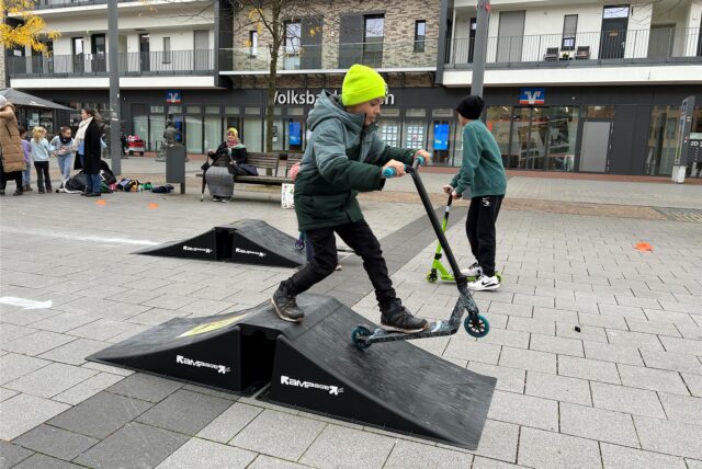 Ein Junge fährt mit einem Roller über eine Rampe.