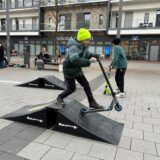 Ein Junge fährt mit einem Roller über eine Rampe.