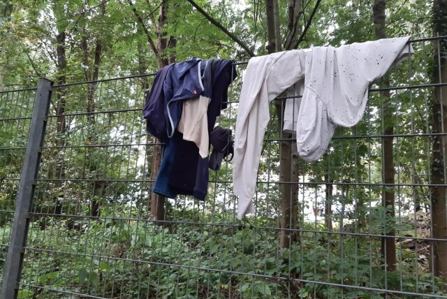 Über einem Stabmattenzaun hängen unordentlich ein paar Bekleidungsstücke