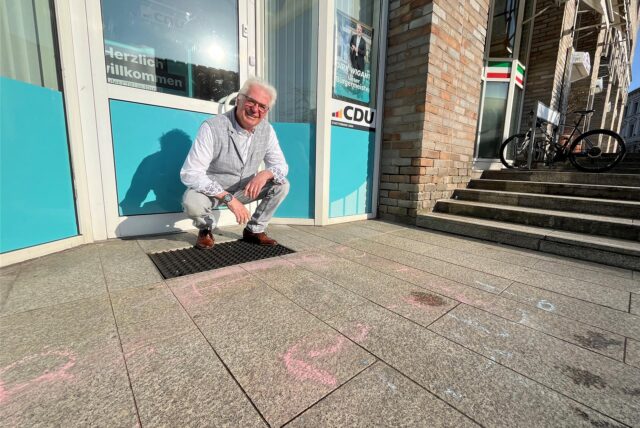 Rudolf Fröhlich (CDU) sitzt vor dem Parteibüro der CDU an der Bahnhofstraße in Unna. Reste vom Kreide-Schmierereien sind noch deutlich erkennbar.