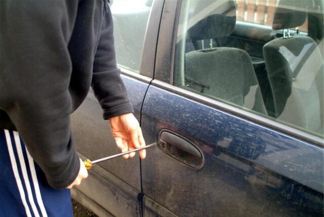Ein Mann (Symbolbild) macht sich an einer Autotür zu schaffen.