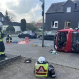 Einsatzkräfte der Feuerwehr stehen an der Bambergstraße in Bergkamen bei einem Auto, das auf der Seite liegt.