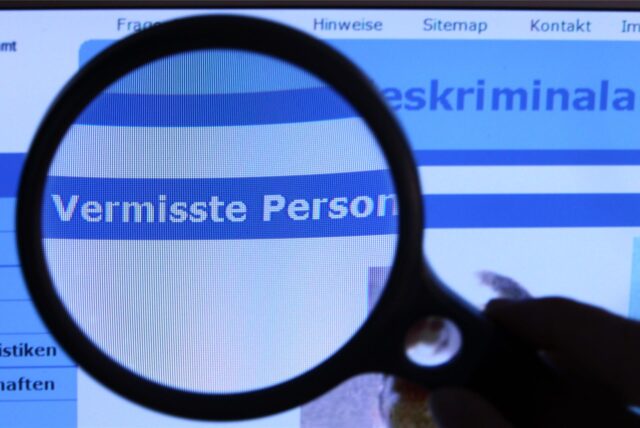 „Vermisste Person“ steht auf einem Computerbildschirm, vor den eine Lupe gehalten wird.