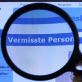 „Vermisste Person“ steht auf einem Computerbildschirm, vor den eine Lupe gehalten wird.
