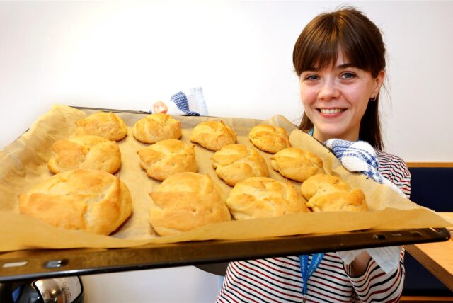 Reporterin Janka Hardenacke hält ein Backblech in den Händen, auf dem Brötchen in Hasenform liegen.