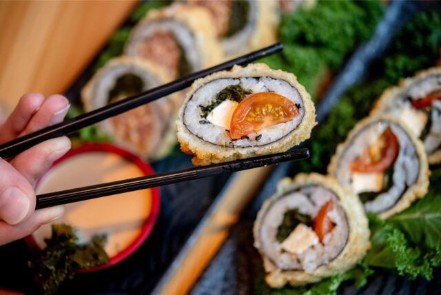 Eine Frau hält mit ihren Stäbchen Sushi mit Grünkohl, Tomaten und Feta im Restaurant Moto Kitchen.