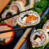 Eine Frau hält mit ihren Stäbchen Sushi mit Grünkohl, Tomaten und Feta im Restaurant Moto Kitchen.