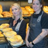 Zwei Bäckereifachverkäuferinnen der Bäckerei Braune in Bergkamen stehen hinter der Theke und lächeln in die Kamera. Sie zeigen ein Blech mit Plunderteilchen.