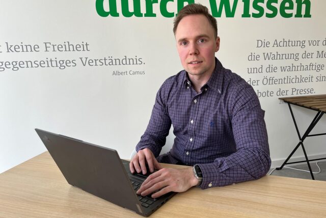 Ein junger Mann sitzt am Schreibtisch und hat die Hände auf dem Laptop.