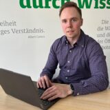 Ein junger Mann sitzt am Schreibtisch und hat die Hände auf dem Laptop.