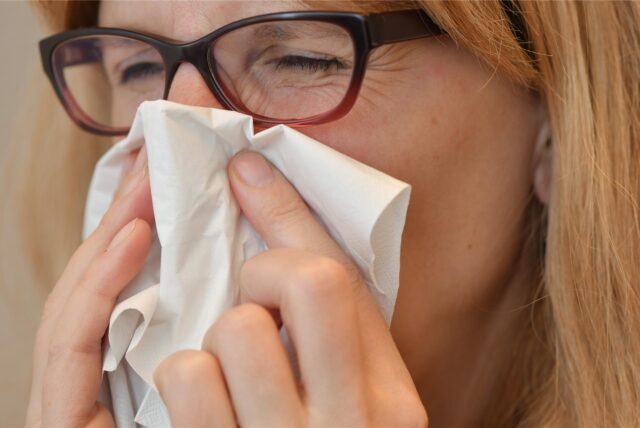 Eine Frau mit Brille putzt sich die Nase.