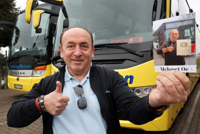 Mehmet Ötegen steht mit einer Autogrammkarte vor seinem Reisebus.