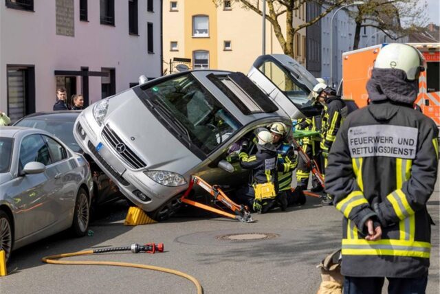 Ein Mercedes liegt über geparkten Autos. Rettungskräfte sichern ein Auto, das schräg auf mehreren geparkten Fahrzeugen zum Stehen gekommen ist.