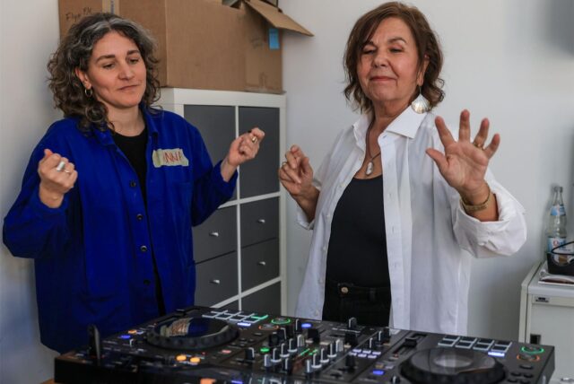 Ingrid Jatho (r), DJ-Schülerin, tanzt beim DJ-Workshop für das Ü70-Publikum mit ihrer Dozentin Anna Cainelli (l) am Mischpult.