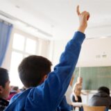 Schulkinder sitzen in einem Klassenraum. Ein Junge zeigt auf.