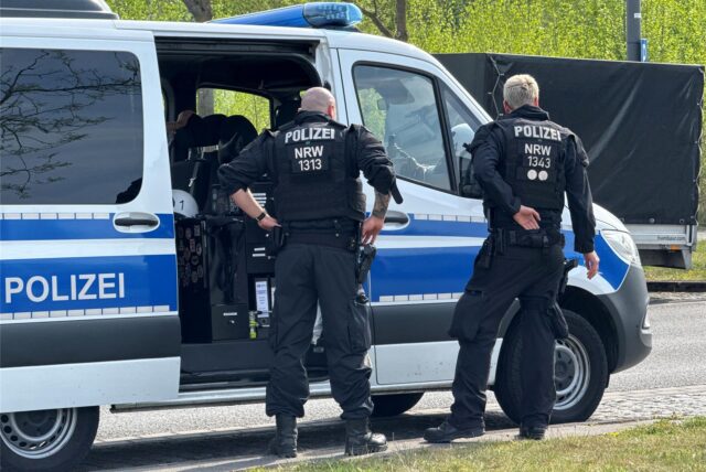 Polizeibeamte stehen vor einem Einsatzwagen.