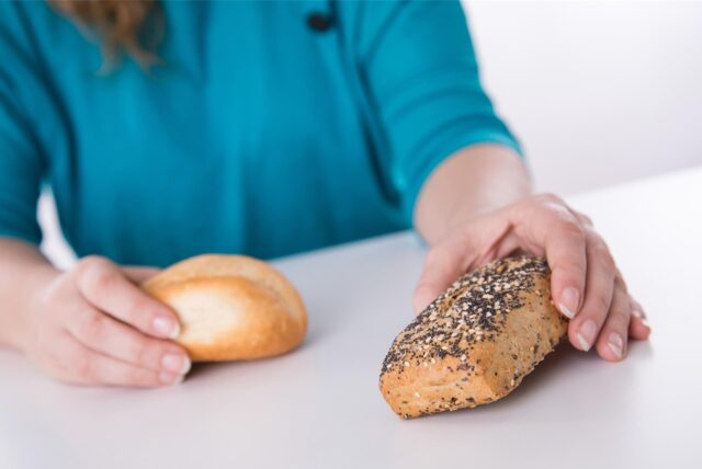 Eine Frau hält ein Brötchen und ein Körnerbrötchen prüfend in den Händen.