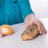 Eine Frau hält ein Brötchen und ein Körnerbrötchen prüfend in den Händen.