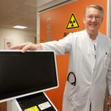Dr. Kai Wiemer steht mit einem Monitor auf dem Flur vor einem Behandlungsraum.