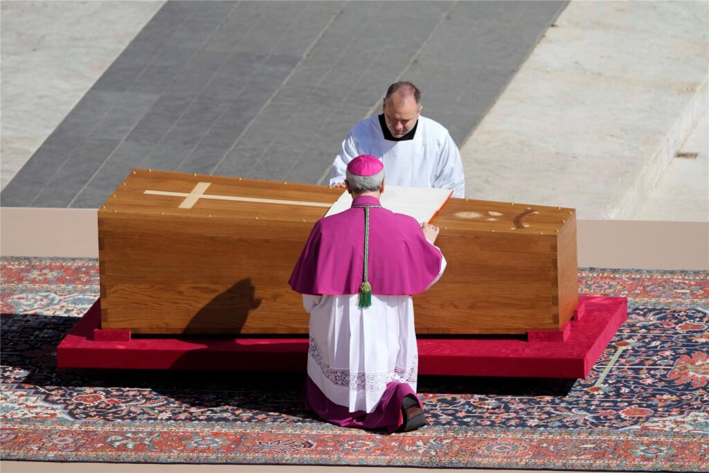Erzbischof Diego Giovanni Ravelli, mit dem Rücken zur Kamera, kniet neben dem Sarg von Papst Franziskus auf dem Petersplatz im Vatikan.

