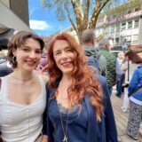 Nicole Schulte vom Weinhaus Schulte mit einem ihrer Models bei der Modenschau bei Kamen blüht auf 2025. Im Hintergrund sind viele Menschen und die Bühne zu sehen.