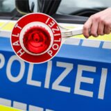 Eine Hand hält eine Polizeikelle, im Hintergrund ein Streifenwagen.