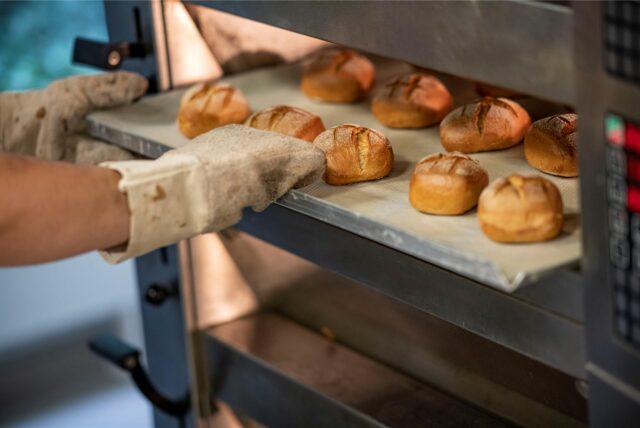 Ein Bäcker holt ein Blech mit frisch gebackenen Brötchen aus dem Ofen.