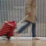 Eine Person in einer beigefarbenen Jacke zieht einen roten Einkaufstrolley hinter sich her.