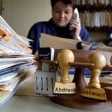 Eine Mitarbeiterin des Landratsamts sitzt telefonierend hinter zahlreichen Akten und Stempeln an ihrem Arbeitsplatz (Archivfoto)