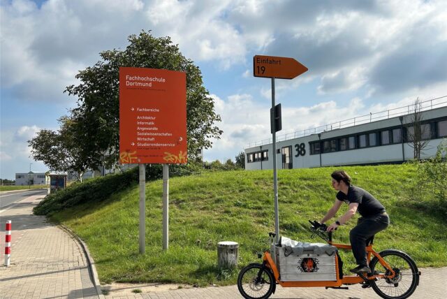 Ein Radfahrer fährt an einem Schild der FH auf dem Campus Nord vorbei.