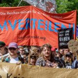 Teilnehmer halten auf einer Mai-Demo mit dem Motto „Superreiche? Superscheiße!“ ein Transparent mit der Aufschrift „Umverteilen!!“.