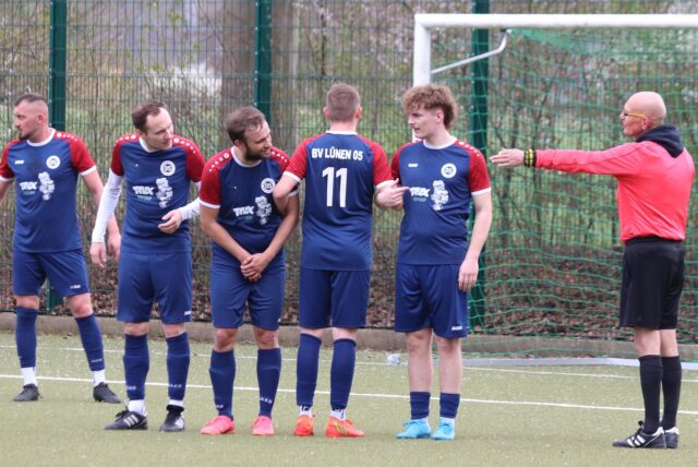 Fußballspieler stehen bereit zum Freistoß und bauen dafür eine Mauer indem sie sich festhalten.