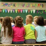 Sechs Grundschüler sitzen an ihrem ersten Schultag in einer Reihe auf einer Bank.