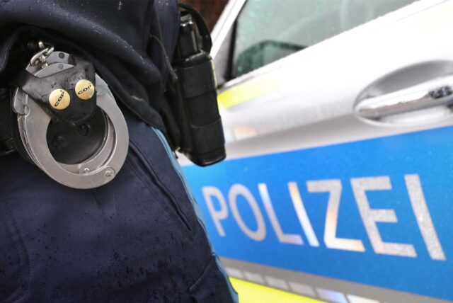 Ein Polizeibeamter steht neben einem Streifenwagen.