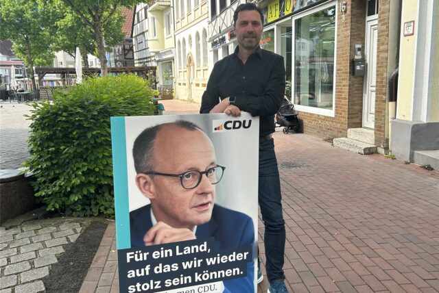 Ralf Eisenhardt hält ein Friedrich-Merz-Plakat.
