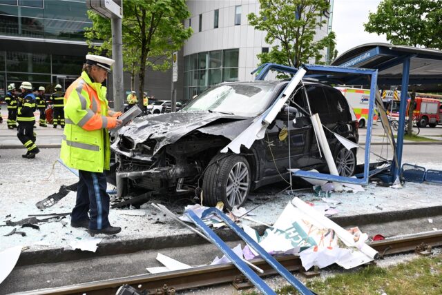 Ein Polizist steht neben dem Unfallfahrzeug in den Glassplittern einer Haltestelle.