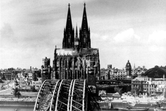 Die Aufnahme von 1945 zeigt den Blick auf den Kölner Dom, der als einziges Bauwerk aus den Trümmern der Stadt hervorragt. Vorn die zerstörte Hohenzollernbrücke.