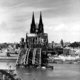 Die Aufnahme von 1945 zeigt den Blick auf den Kölner Dom, der als einziges Bauwerk aus den Trümmern der Stadt hervorragt. Vorn die zerstörte Hohenzollernbrücke.